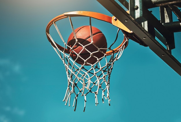 Gol de baloncesto y objetivo en la canasta para el entrenamiento de partidos deportivos en la cancha atlética al aire libre Puntaje de objetivo y ganador con clavada de pelota en la red en la práctica de competencia desde un ángulo bajo con cielo azul