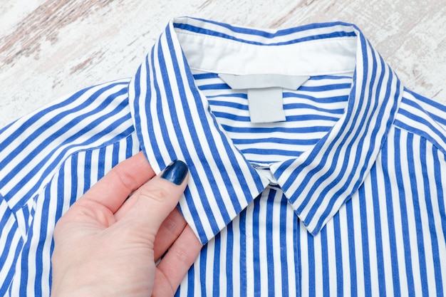 Gola de camisa listrada de azul e branco em uma mão feminina. fechar-se. na moda.