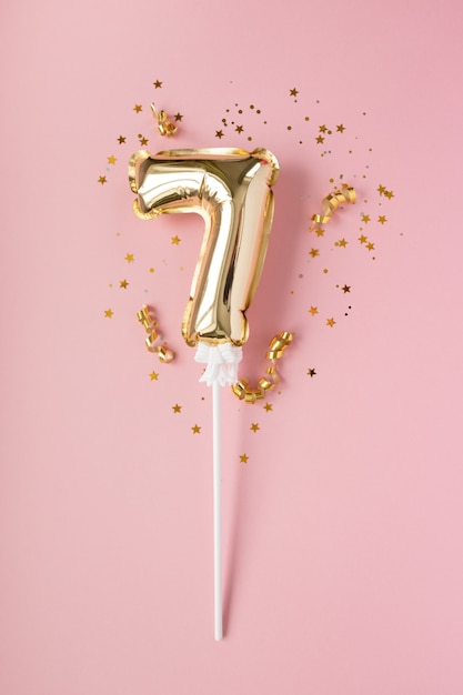Gold aufblasbare Nummer 7 auf einem Stock Gold Konfetti auf einem rosa Hintergrund. Konzept eines Feiertags, Geburtstags, Jahrestages.