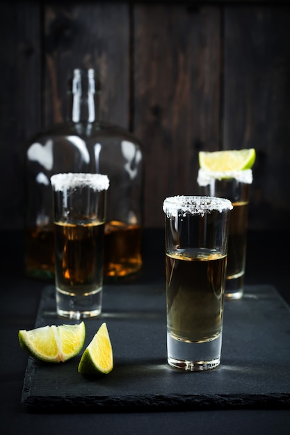 Gold Tequila mit Limette und Salz auf einer dunklen Oberfläche. Selektiver Fokus.