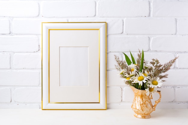 Gold verzierter Rahmen mit Kamille und Gras in goldener Vase