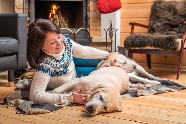 Golden Labrador Retrievers yacen junto a una mujer asiática de mediana edad sobre una manta frente a la chimenea de una casa de campo.