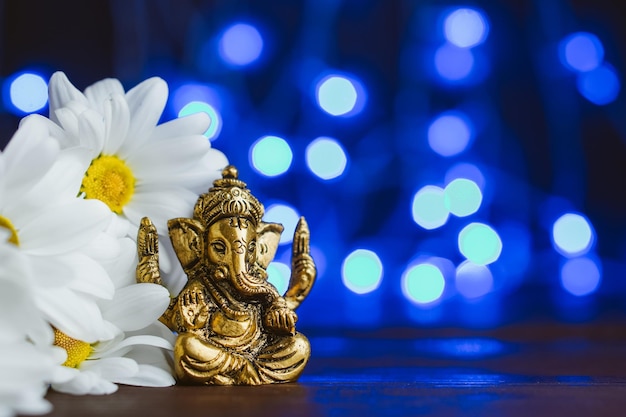 Golden Lord Ganesha Skulptur in Gänseblümchen über blau beleuchtetem Hintergrund Platz für Text kopieren