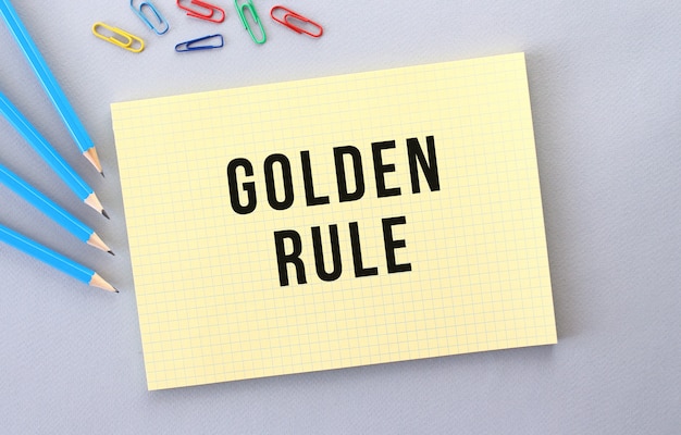 Golden rule text im notizbuch auf grauem hintergrund neben stiften und büroklammern. konzept.