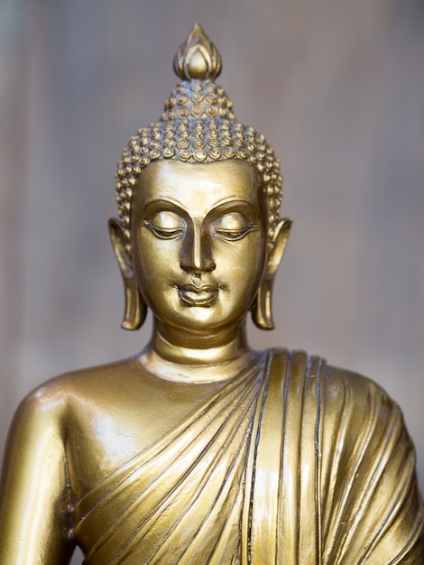 Goldene antike Buddha-Statue. Der Hintergrund ist hellgrau.