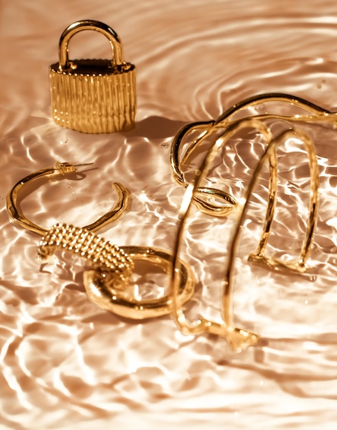 Foto goldene armbänder ohrringe ringe schmuck auf goldenem wasser hintergrund luxus glamour und urlaubsschönheitsdesign für schmuckmarkenanzeigen