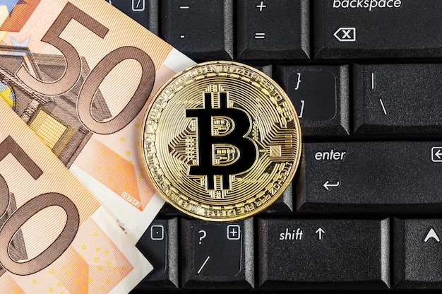 Goldene Bitcoin mit Euro-Scheinen auf Laptop-Tastatur E-Commerce-Konzept