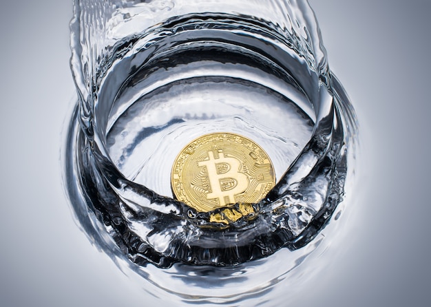 Goldene Bitcoin-Münze mit Wasserspritzen.