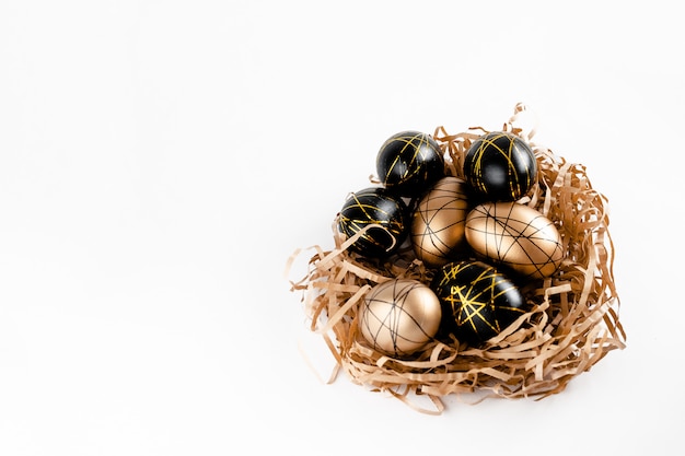 Goldene dekorierte Ostereier im Nest auf weißem Hintergrund. Minimaler Kopierraum für Osterkonzepte für Text. Horizontale Draufsicht, Flatlay.