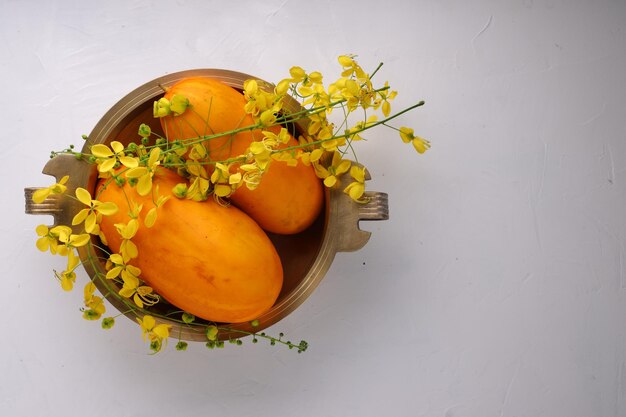 Goldene Duschblume und gelbe Gurkearrangiert in einem traditionellen Messinggefäß oder einer Urule auf dem weißen strukturierten Hintergrund