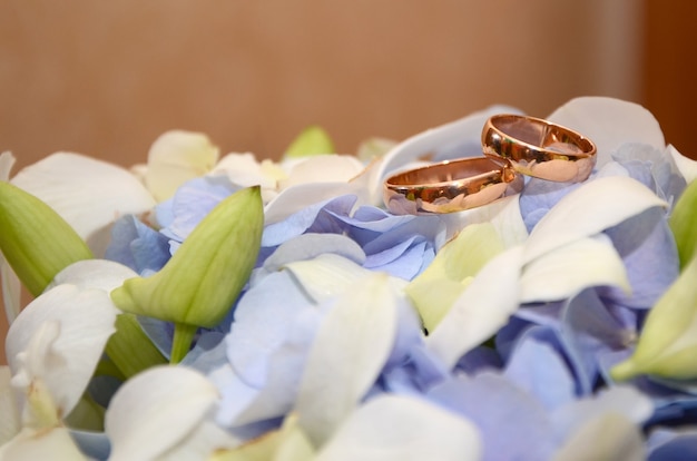 Goldene Eheringe auf einer weißen Blume eines schönen Brautstraußes mit lila Blumen hautnah