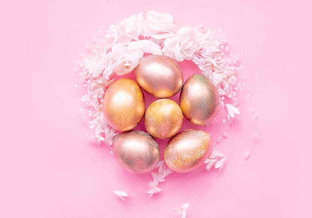 Goldene Eier in einem Blumennest auf rosa Hintergrund Osterkonzept mit Platz für Text