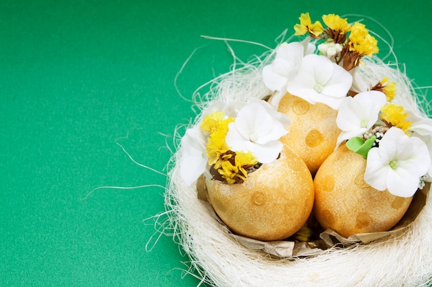 Goldene Eier mit Blumen in einem Nest auf grüner Oberfläche