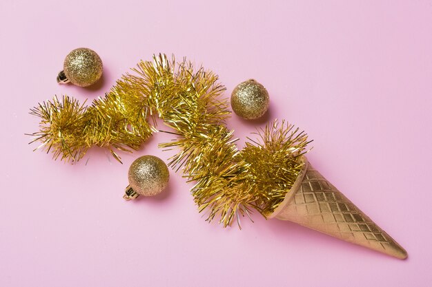 Goldene Eistüte, goldenes Lametta und drei goldene Weihnachtskugeln, Feiertagskonzept