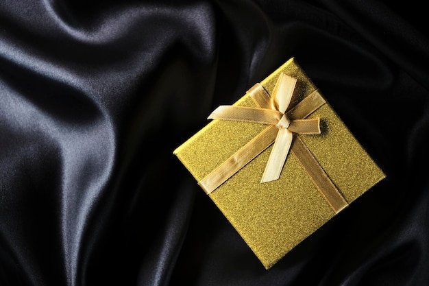Goldene Geschenkbox mit Schleifenhintergrund mit schwarzem Seidenstoff