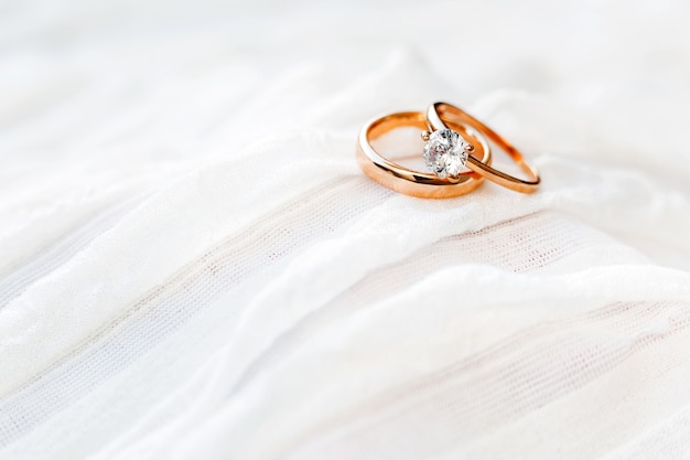 Goldene Hochzeit Ringe mit Diamanten liegen auf weißem Stoff. Symbol für Liebe und Ehe.