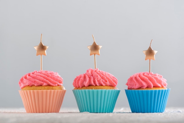 Goldene Kerzen in Sternform auf Cupcakes mit rosa Buttercreme-Zuckerguss. Cupcakes zum Geburtstag. Partyessen. Nahansicht