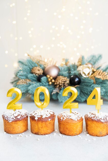 Goldene Kerzen mit der Nummer 2024 auf den Cupcakes Frohe Weihnachten und frohes Neujahr