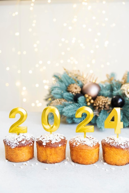 Goldene Kerzen mit der Nummer 2024 oben auf Cupcakes mit Weihnachtsdekoration und Bokeh-Leuchten im Hintergrund Frohe Weihnachten und frohes Neujahr Feier Stimmung Glückliche Feiertage Festliche Bäckerei