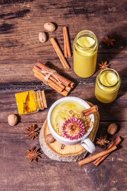 Goldene Kurkumamilch mit Eis. Zimt, Muskatnuss, Anisgewürze. Gesundes Frühstücksgetränkkonzept am Morgen. Ein modernes hartes Licht, dunkler Schatten, alter Holztisch, Draufsicht