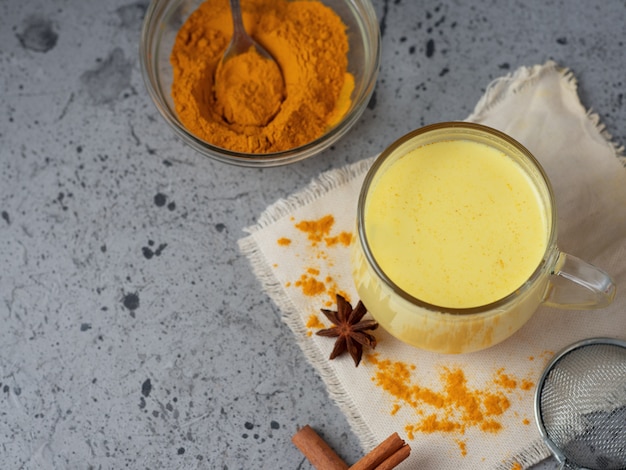 Goldene Milch der indischen Gewürzgelbwurz in einem Becher auf einer dunklen Steintabelle