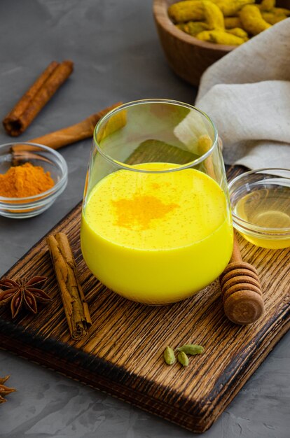 Goldene Milch in einem Glas auf einem Holzbrett mit Honig und anderen Gewürzen. Ein gesundes Getränk aus Milch und Kurkuma.