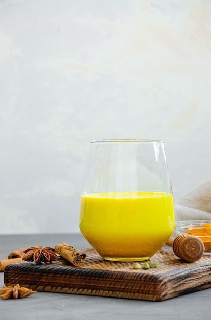 Goldene Milch in einem Glas auf einem Holzbrett mit Honig und anderen Gewürzen