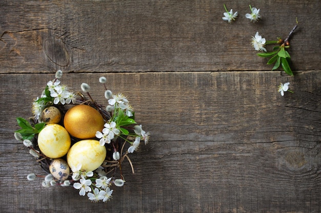 Goldene Ostereier in einem Nest mit Weidenzweigen und Frühlingsblumen Draufsicht