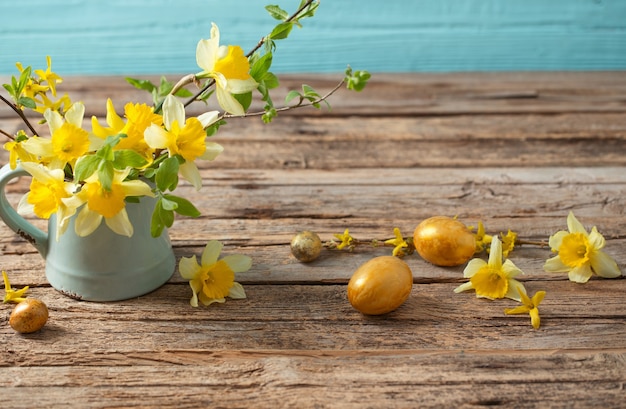 Goldene Ostereier und gelbe Blumen auf hölzernem Hintergrund