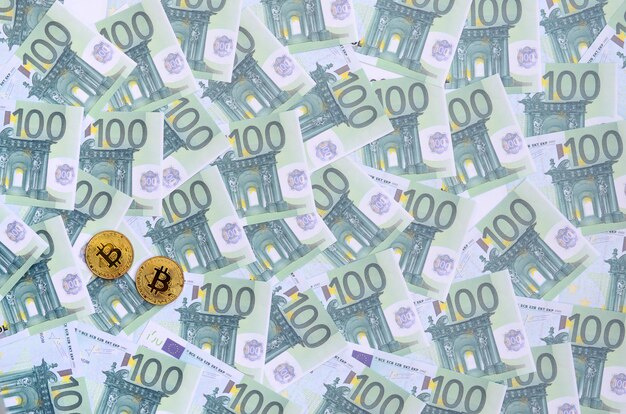 Goldene physische bitcoins liegt auf einer reihe grüner währungsbezeichnungen von 100 euro