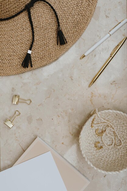 Goldene Strohhut-Accessoires auf Marmortisch mit leerem Kopierraum. Stilvolle Mode-Flachlage, Draufsicht, minimalistische Home-Office-Schreibtisch-Arbeitsplatzvorlage