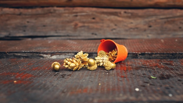 Goldene Tannenzapfen und Eicheln, die aus einem winzigen orangefarbenen Eimer fließen
