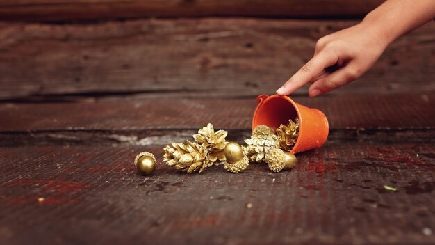 Goldene Tannenzapfen und Eicheln, die aus einem winzigen orangefarbenen Eimer fließen