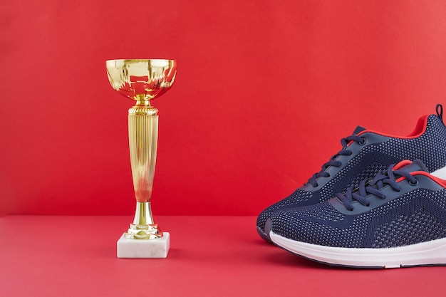 Goldene Trophäe und Laufschuhe auf rotem Hintergrund Schuhe und goldene Trophäe