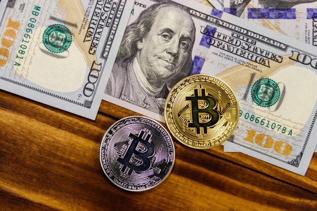 Goldene und silberne Bitcoins und Hundert-Dollar-Scheine auf Holzschreibtisch