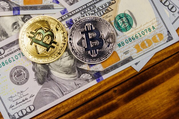 Goldene und silberne Bitcoins und Hundert-Dollar-Scheine auf Holzschreibtisch