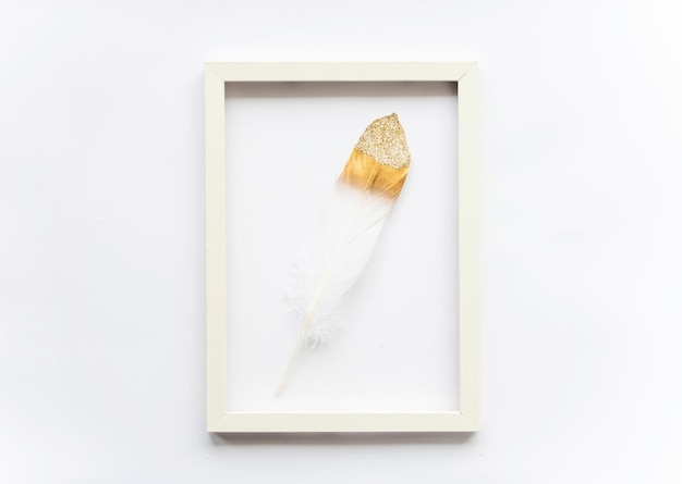 Goldene Vogelfeder in einem Rahmen auf weißem Hintergrund mit Kopierplatz für Text Minimales Konzept Ansicht von oben Weicher selektiver Fokus der Osterkarte