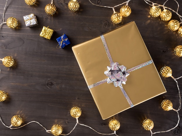 Goldene Weihnachtsgeschenkbox mit goldenen Weihnachtslichtern auf hölzernem Hintergrund. Kleine Geschenke.