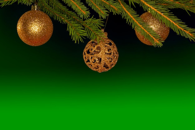 Goldene Weihnachtskugeln hängen an einem Weihnachtsbaum auf grünem Hintergrund.