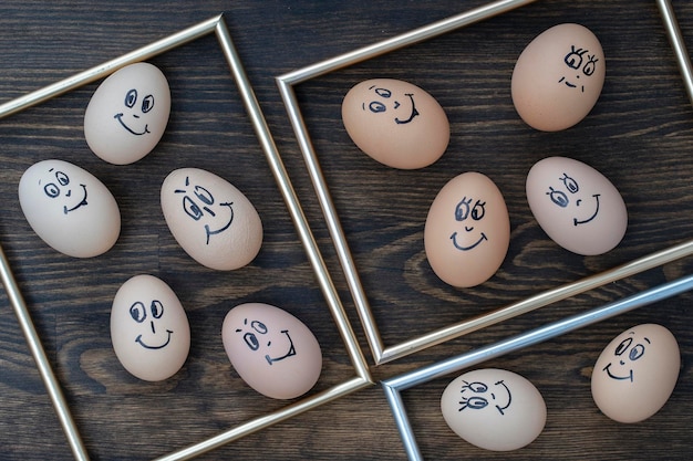 Goldener Bildrahmen und viele lustige Eier, die auf dunklem Holzwandhintergrund lächeln Eier Familie Emotion Gesicht Porträt Konzept lustiges Essen