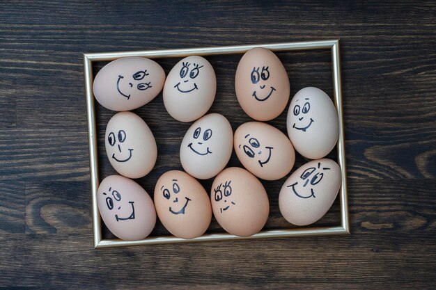 Goldener Bildrahmen und viele lustige Eier, die auf dunklem Holzwandhintergrund lächeln Eier Familie Emotion Gesicht Porträt Konzept lustiges Essen