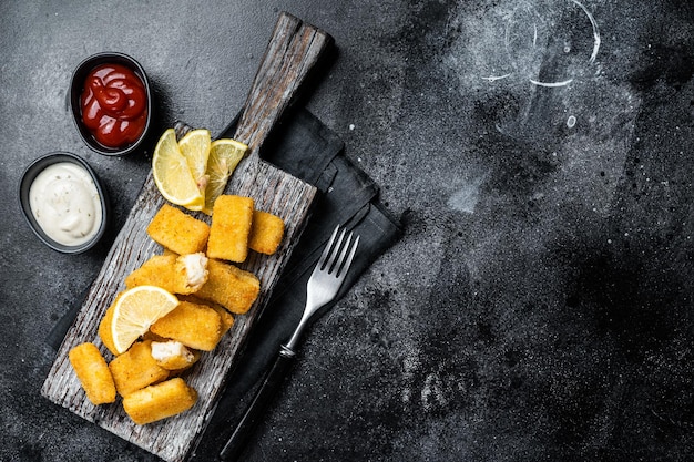 Goldener Braten Fischstäbchen Finger mit Soße auf einem Holzbrett Schwarzer Hintergrund Draufsicht Kopierbereich