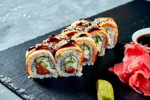 Goldener Drache der Sushi-Rolle mit Aal, Lachs, Philadelphia-Käse und Unagi-Sauce auf einem schwarzen Schieferbrett.