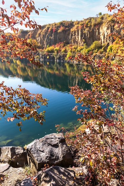 Goldener Herbst mit bunten Bäumen im alten überfluteten Steinbruch. Felsen, See und gelbe Bäume