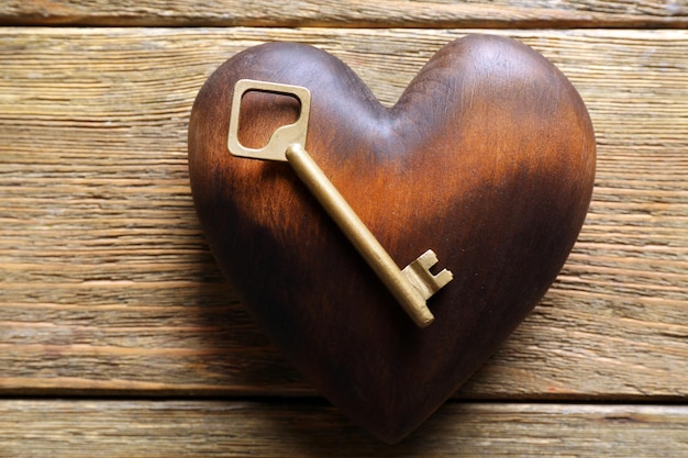 Goldener Schlüssel mit braunem Herzen auf Holzhintergrund