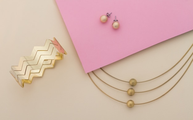 Goldener Schmuck stellte auf rosa und beige Hintergrund ein