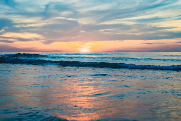 Goldener Sonnenuntergang über dem Strand mit Wellenspritzern im Sommer von Thailand