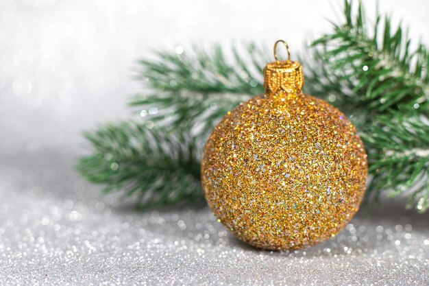 Goldener Weihnachtsball mit Weihnachtsbaumzweigen auf Glitzerhintergrund.