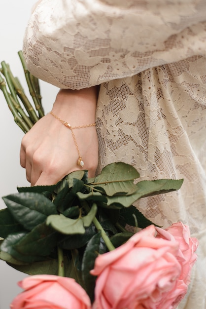 goldenes Armband mit einer Perle in der Hand des Mädchens. Ein Mädchen in einem Spitzenkleid hält einen Strauß Pfingstrosen mit einem trendigen Armband in der Hand.
