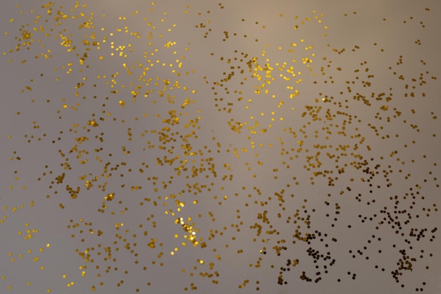 Goldenes Glitzerkonfetti auf grauem Hintergrund. Glänzende Partikel, dekorativer abstrakter Hintergrund. Party, Frohe Weihnachten, Frohes Neues Jahr.